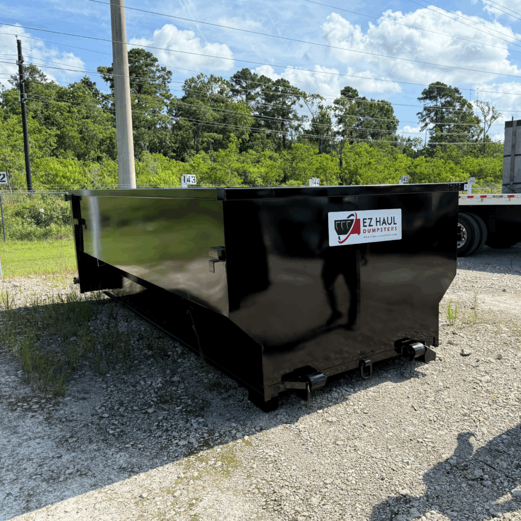 Black EZ Haul Dumpsters roll-off dumpster on a gravel lot, with trees and power lines in the background
