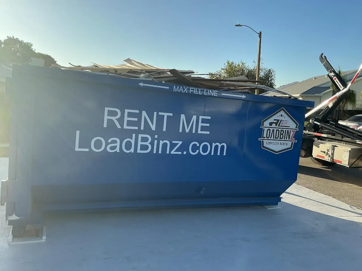 A blue LoadBinz dumpster parked on a residential driveway, clearly displaying the 'Max Fill Line' marking on its side to guide safe loading.