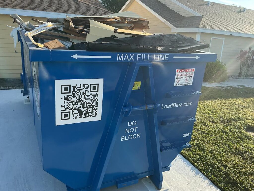 A LoadBinz dumpster parked in a driveway, demonstrating an overfilled container that exceeds the marked 'Max Fill Line'.