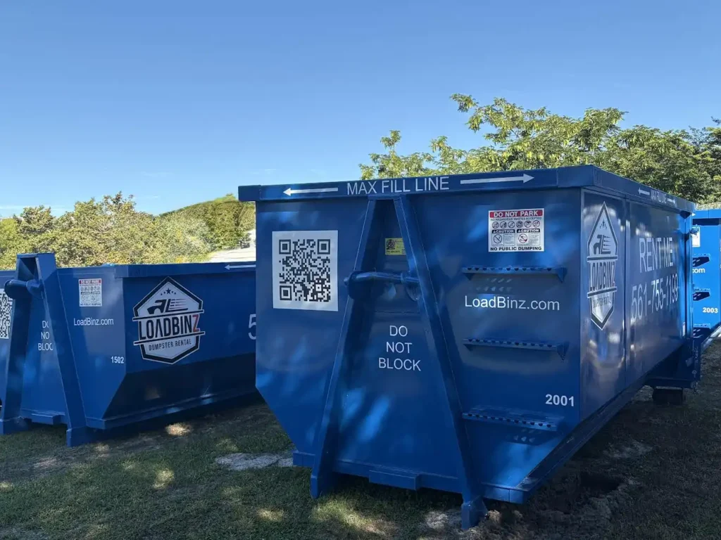 A row of blue LoadBinz rental dumpsters featuring 'Max Fill Line' markers, QR codes, and contact information for local dumpster services.