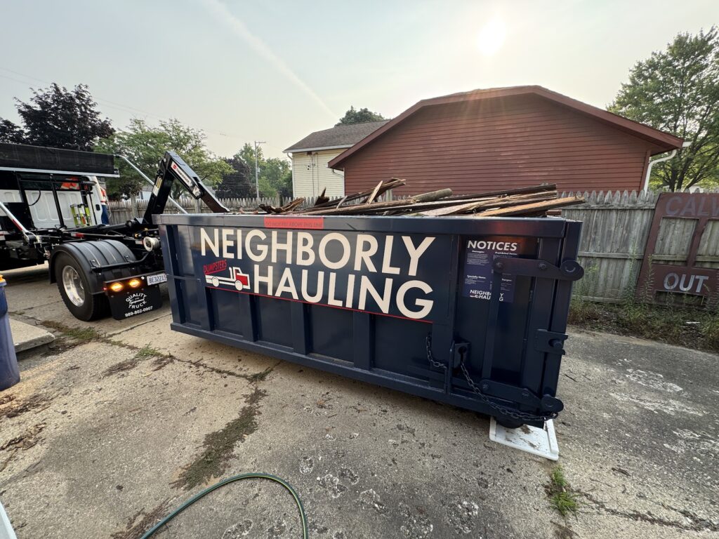 Neighborly Hauling 12-yard dumpster rental in Grand Rapids driveway loaded with wood debris, placed on Rolliskate pads