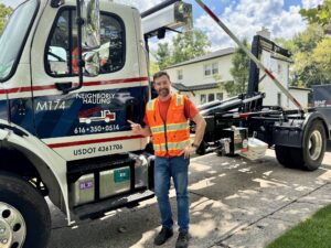 Neighborly Hauling driver with hook-lift dumpster truck in Grand Rapids driveway