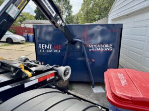 Neighborly Hauling dumpster being positioned close to a garage using a hook-lift truck in a tight residential driveway.
