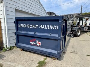 Neighborly Hauling dumpster placed tightly beside a residential garage using a hook-lift truck.