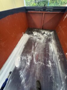 Dumpster interior being cleaned with a pressure washer after wet paint spilled inside.
