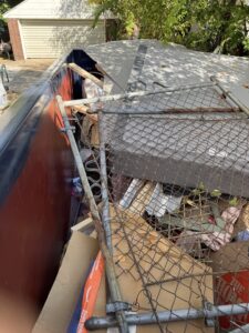 Overfilled Neighborly Hauling dumpster containing old fencing panels, roof debris, cardboard, and assorted household junk.