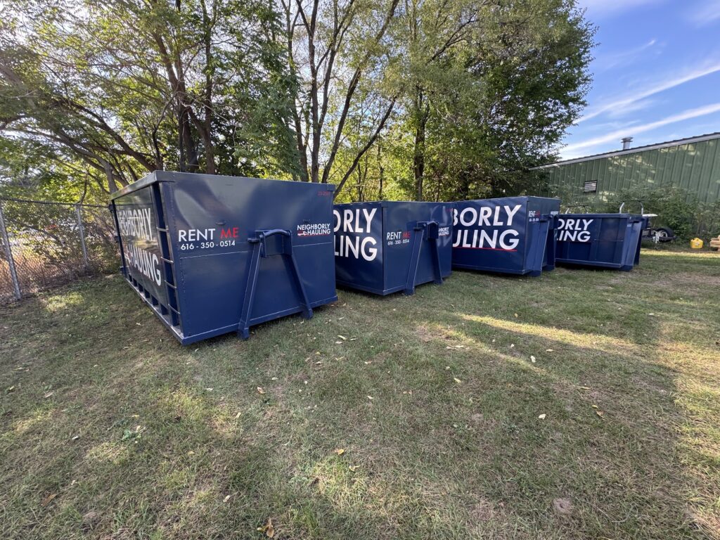Multiple Neighborly Hauling dumpsters lined up outdoors, ready for rental on a grassy lot.