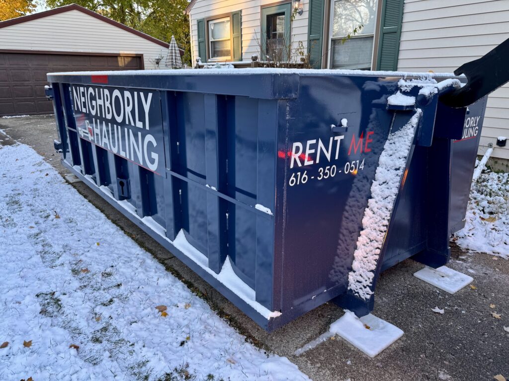 Neighborly Hauling dumpster placed on protective pads in a snowy residential driveway during winter.