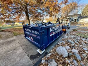 Neighborly Hauling truck picking up a full dumpster loaded with debris in a residential neighborhood during fall.