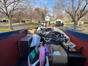 Dumpster filled with household junk, toys, boxes, and miscellaneous cleanout items in a residential neighborhood.