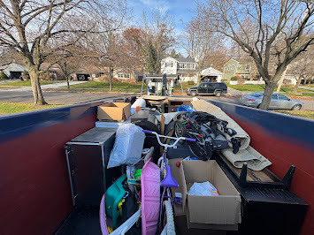 Dumpster filled with household junk, toys, boxes, and miscellaneous cleanout items in a residential neighborhood.